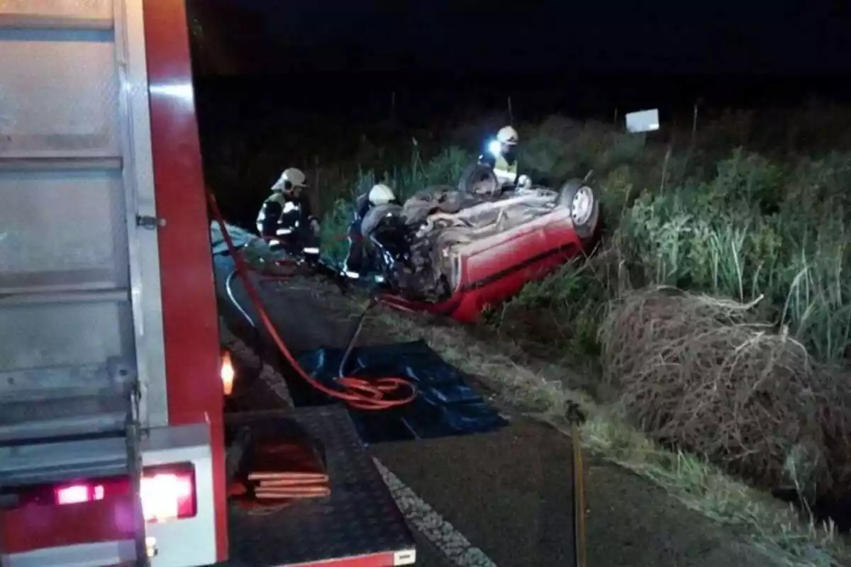 Accident amb un cotxe del revés i els bombers actuant al cotxe