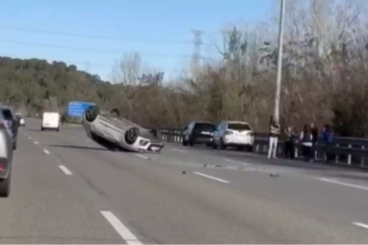 Coche volcado en una carretera con varios vehículos y personas al fondo.