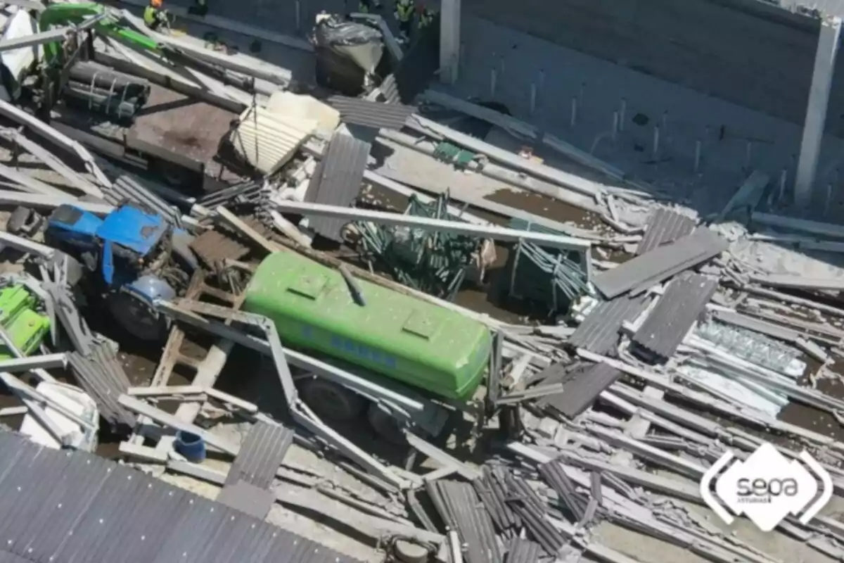 Vista aèria d’un col·lapse estructural en una nau industrial amb runa de metall i vehicles atrapats entre les restes Vista aèria d’un col·lapse estructural en una nau industrial amb runa de metall i vehicles atrapats entre les restes