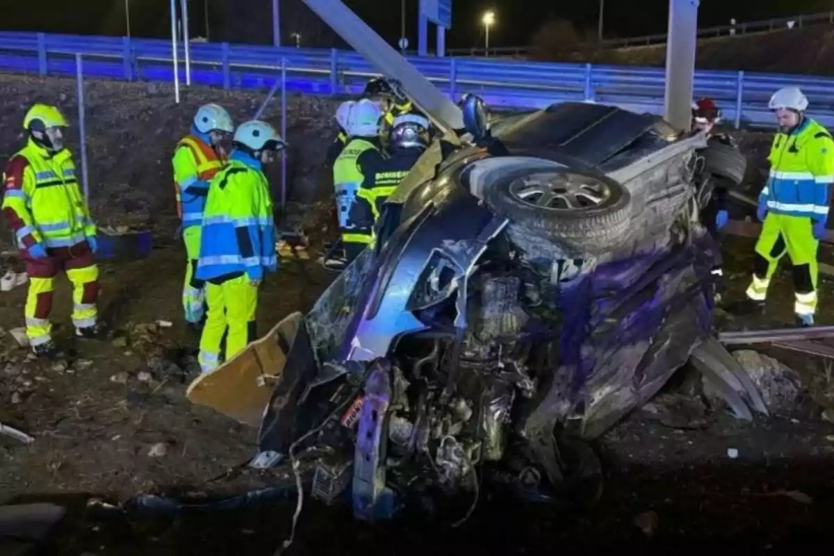 Un grupo de rescatistas con equipo de protección observa un automóvil volcado y dañado en un accidente nocturno.