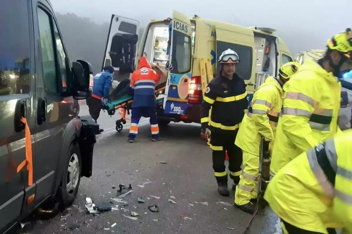 Un grup de rescatistes i personal mèdic atén una emergència a la carretera amb una ambulància i un vehicle danyat.