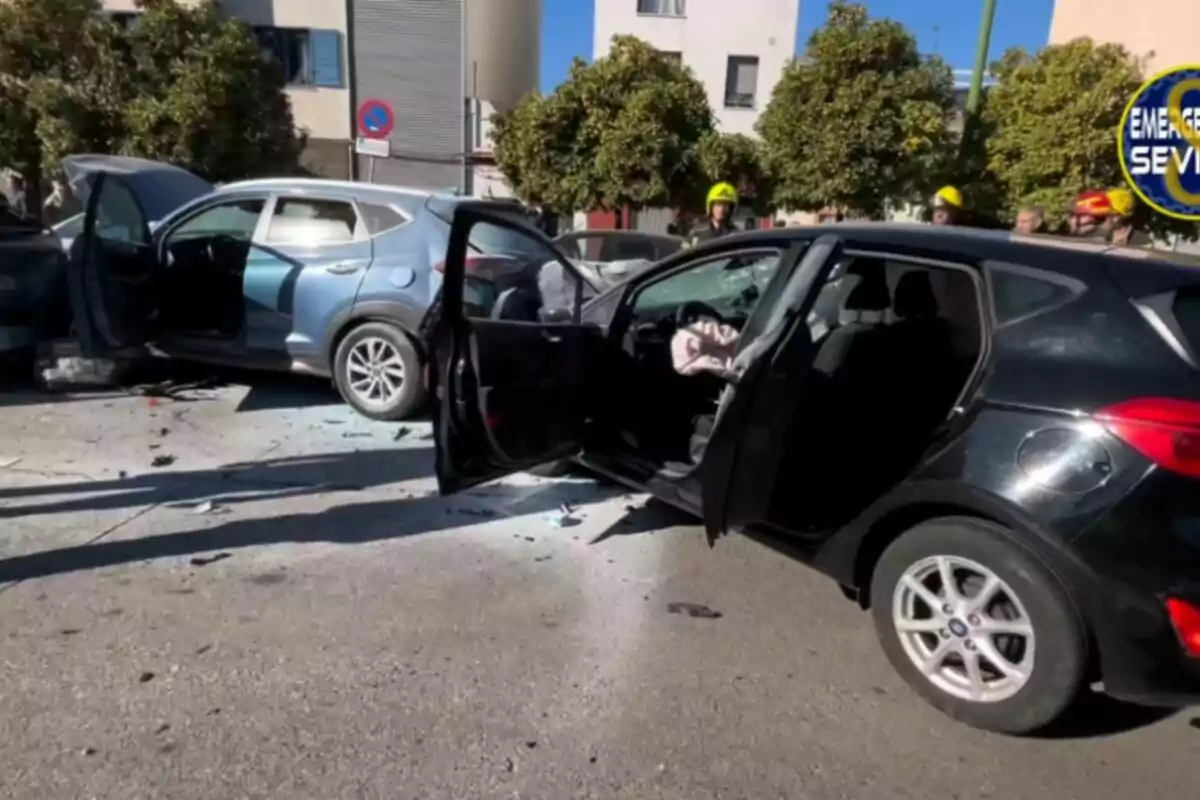 Dos cotxes involucrats en un accident amb les portes obertes i els danys visibles en un carrer urbà amb arbres i edificis al fons.