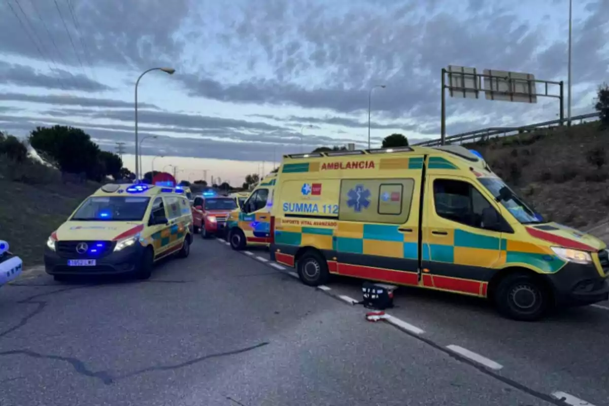 Diverses ambulàncies i vehicles d'emergència estan estacionats en una carretera cap al tard amb llums blaves encesos.