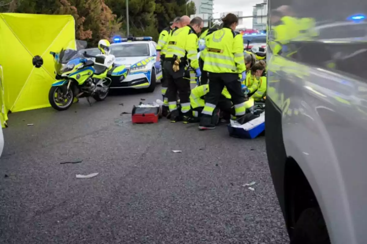 Un grup de paramèdics atén una emergència a una carretera, envoltats de vehicles de policia i una motocicleta.