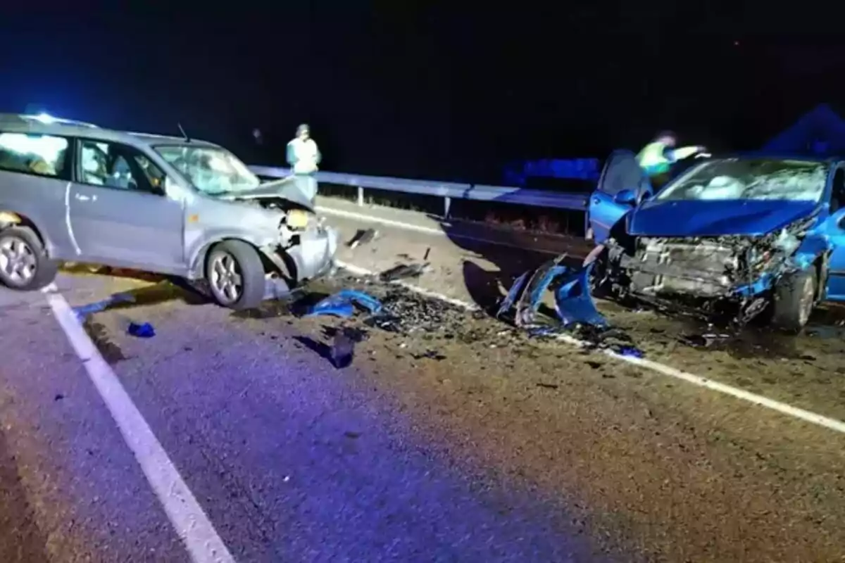 Dos cotxes xocats en una carretera a la nit amb runes escampades i persones observant.