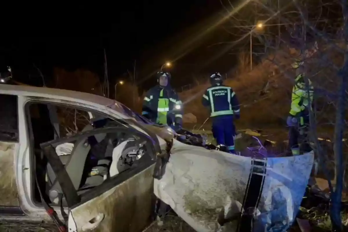 Un cotxe accidentat a la nit amb bombers treballant al lloc.