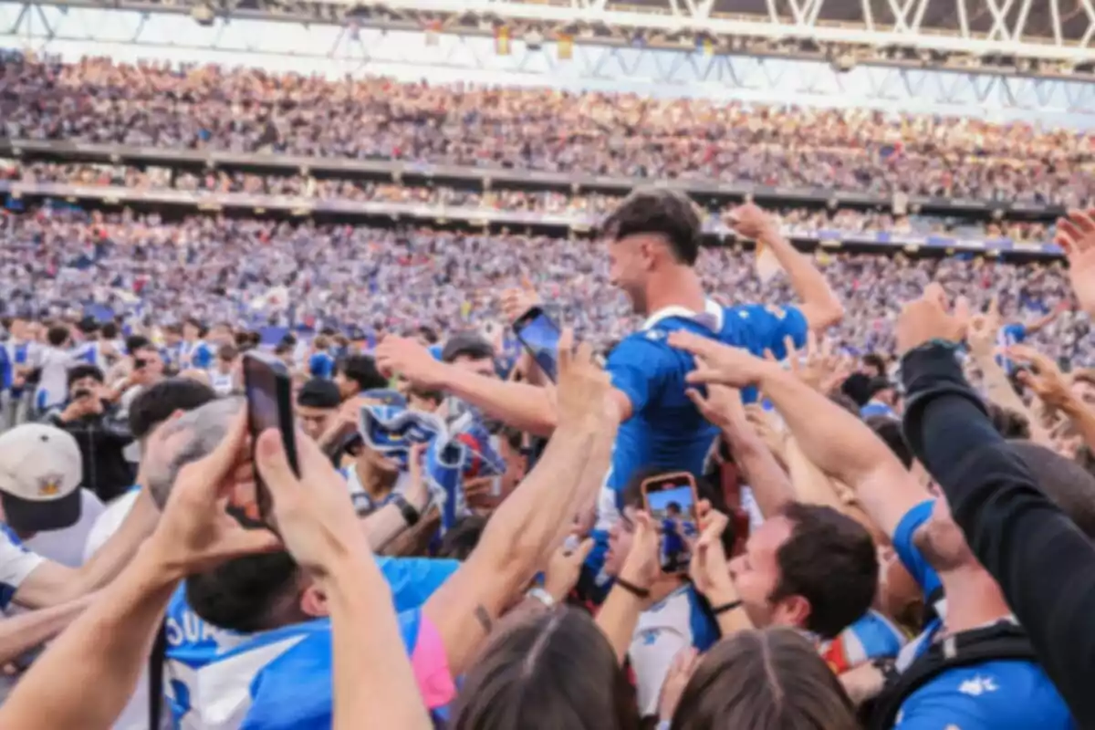 Aficionats celebren amb un jugador al camp d’un estadi ple durant un partit de futbol. Aficionats celebren amb un jugador al camp d’un estadi ple durant un partit de futbol.