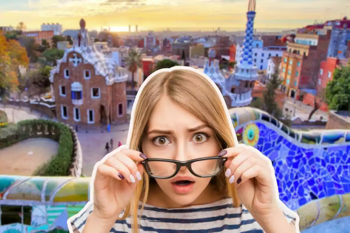 Una dona amb expressió de sorpresa sosté les ulleres davant d'un fons d'un parc colorit i arquitectònicament distintiu.