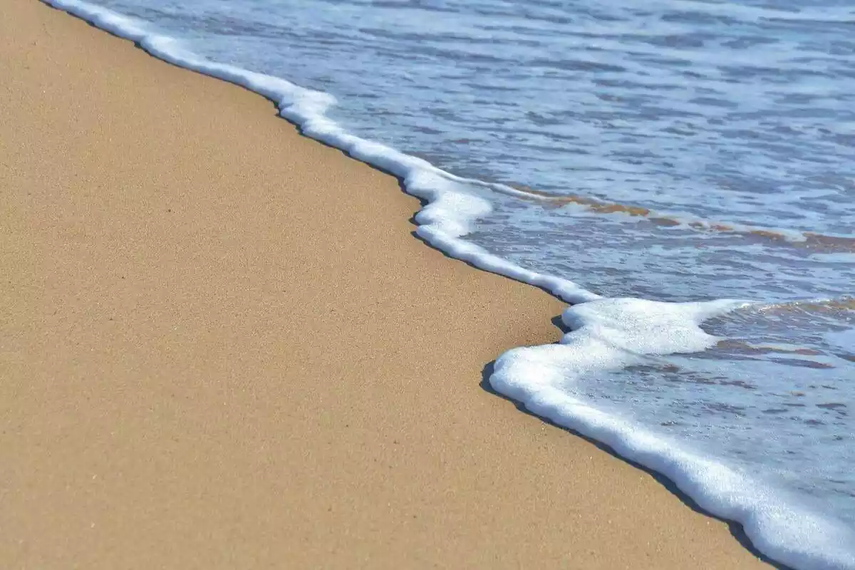 Plànol curt de l'aigua arribant a la vora del mar a la platja