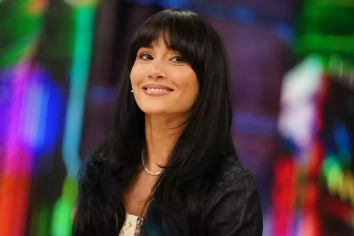Aitana amb cabell llarg i fosc amb serrell somrient davant d’un fons colorit i desenfocat a ‘El Hormiguero’.