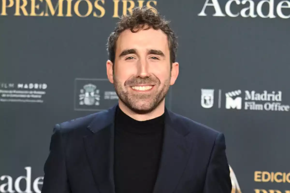 Aitor Albizua somrient amb barba i cabell arrissat porta un vestit fosc i està en un esdeveniment amb un fons que té logotips i text. Aitor Albizua somrient amb barba i cabell arrissat porta un vestit fosc i està en un esdeveniment amb un fons que té logotips i text.