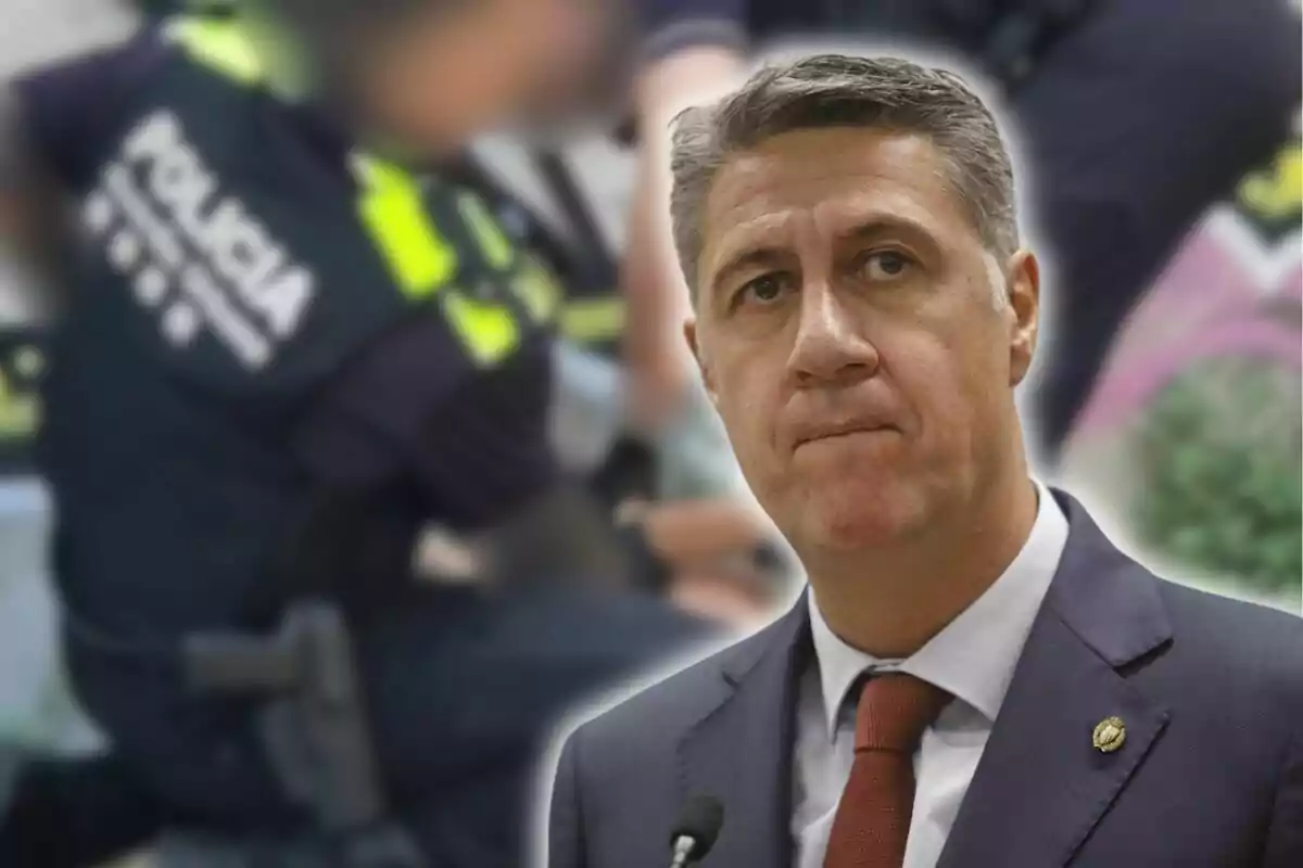 Un home amb vestit i corbata apareix en primer pla amb una expressió seriosa mentre al fons s’observen policies desenfocats realitzant una intervenció.