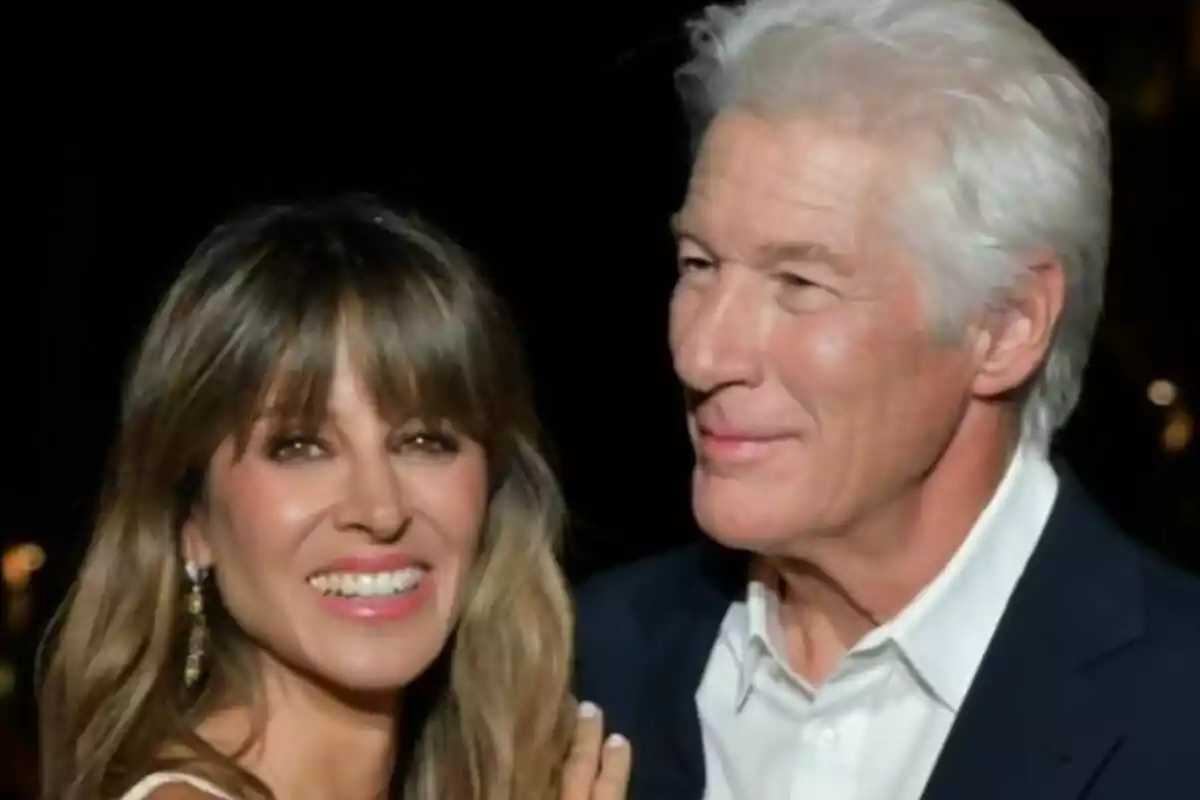 Una pareja -formada por Alejandra Silva y Richard Gere- sonríe y posa junta en un evento elegante con fondo oscuro. Una pareja -formada por Alejandra Silva y Richard Gere- sonríe y posa junta en un evento elegante con fondo oscuro.