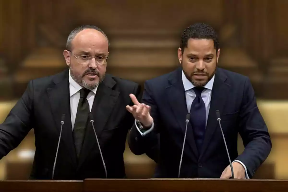 Dos homes amb vestits foscos parlant en un faristol amb micròfons davant d'un fons de fusta.