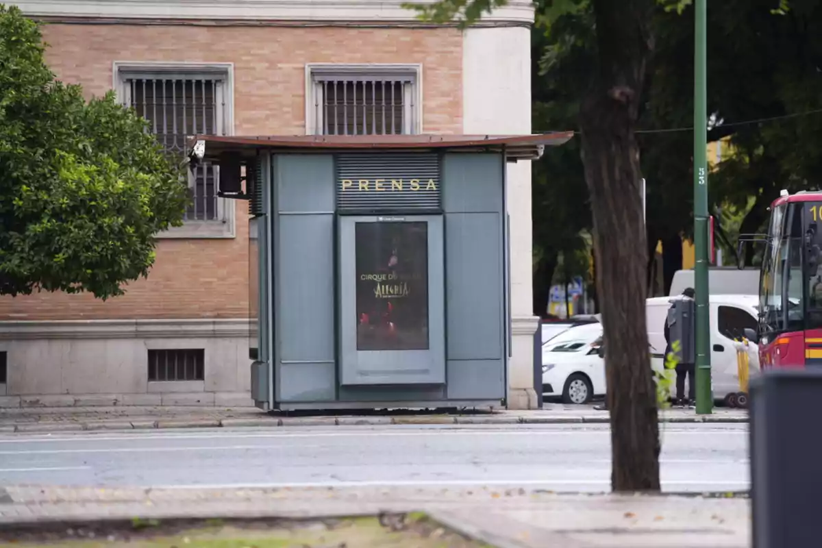 Quiosc de premsa en un carrer amb un cartell del Cirque du Soleil i un autobús vermell a la dreta.