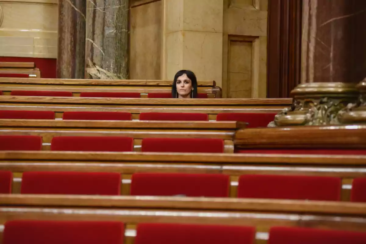 Una dona asseguda sola en un auditori amb seients vermells i detalls de fusta.