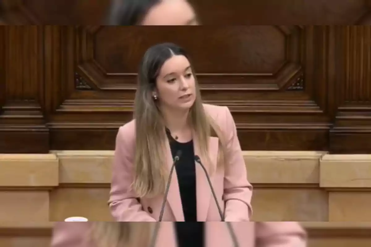 Una dona amb jaqueta rosa parla en un podi de fusta.