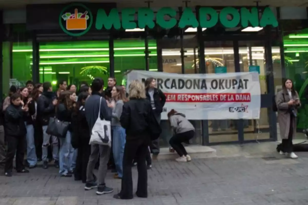 Un grup de persones es reuneixen davant l?entrada d?un supermercat Mercadona, on hi ha una pancarta amb un missatge de protesta.