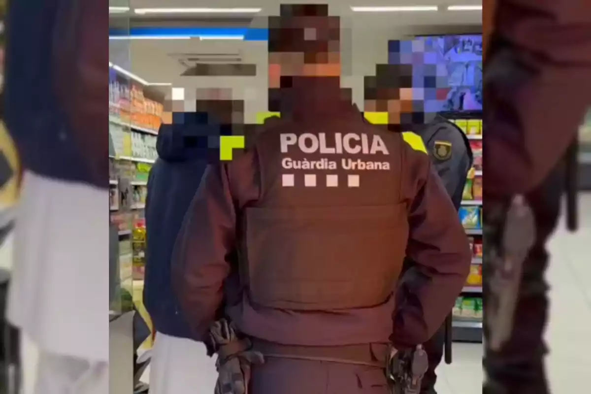 Un agente de la Guardia Urbana de espaldas en una tienda, acompañado de otras personas con rostros pixelados.