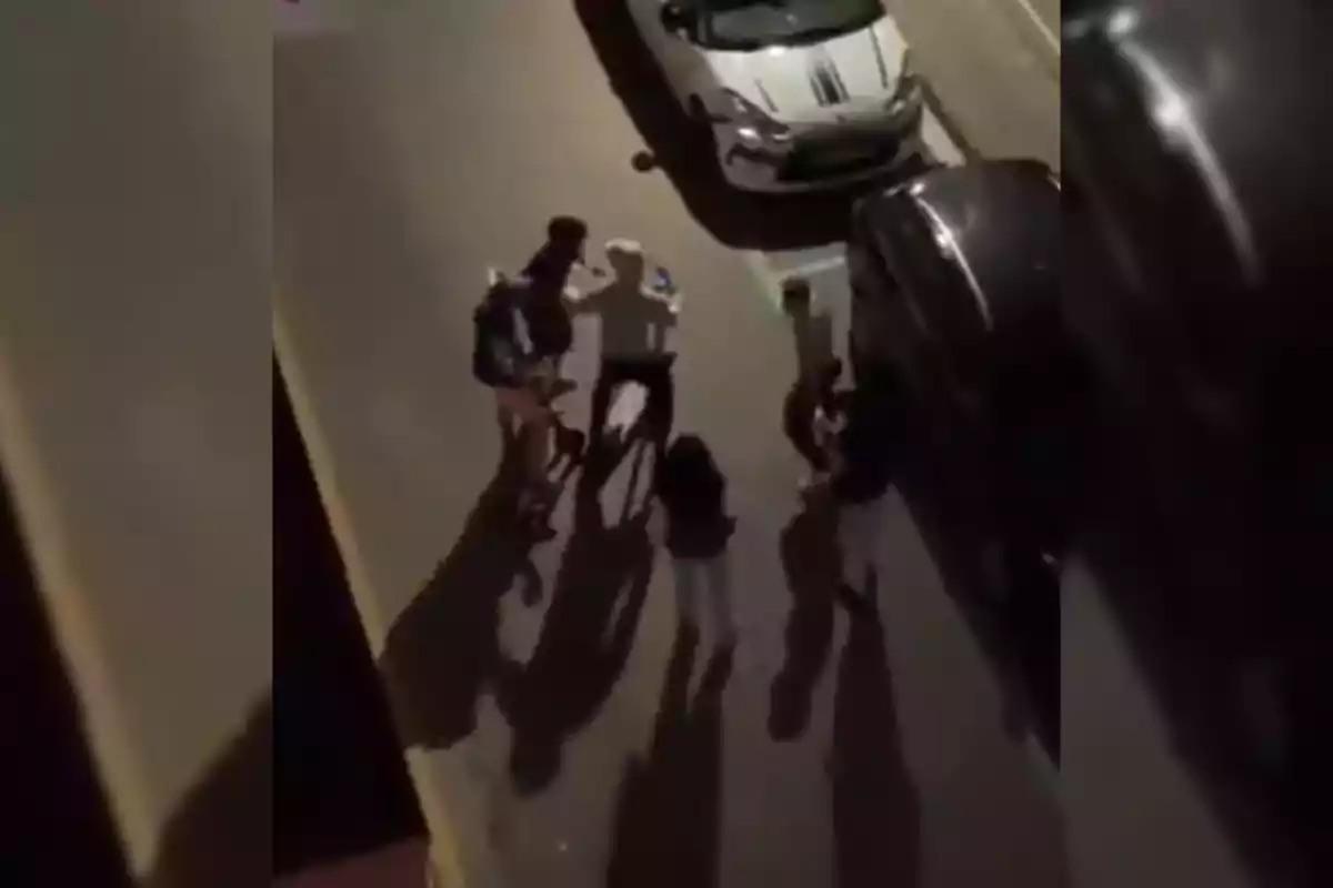 Un grup de persones dretes en un carrer al costat de diversos cotxes estacionats.