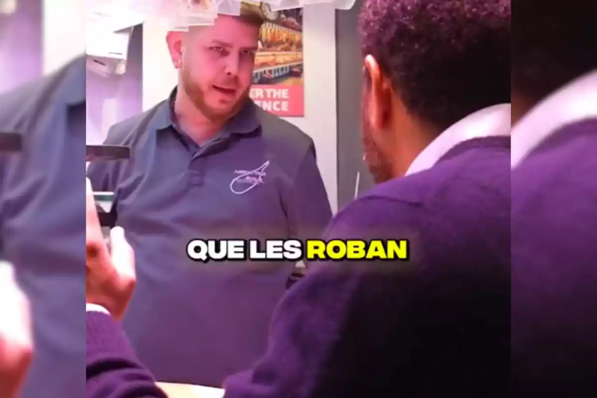 Dues persones conversen en un taulell, una d'elles porta una samarreta amb un logotip i l'altra està d'esquena; al centre de la imatge hi ha un text que diu "QUE ELS ROBEN".