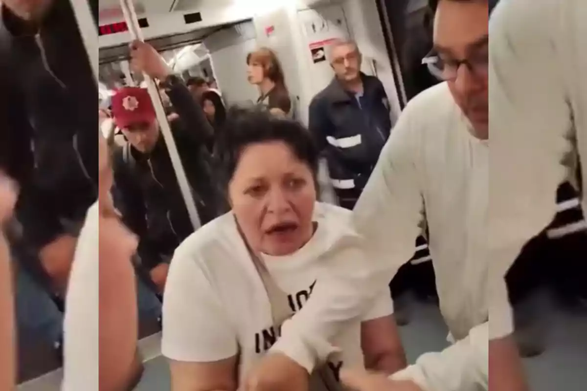 Una dona amb expressió preocupada està sent assistida per un home en un vagó de metro ple de passatgers.