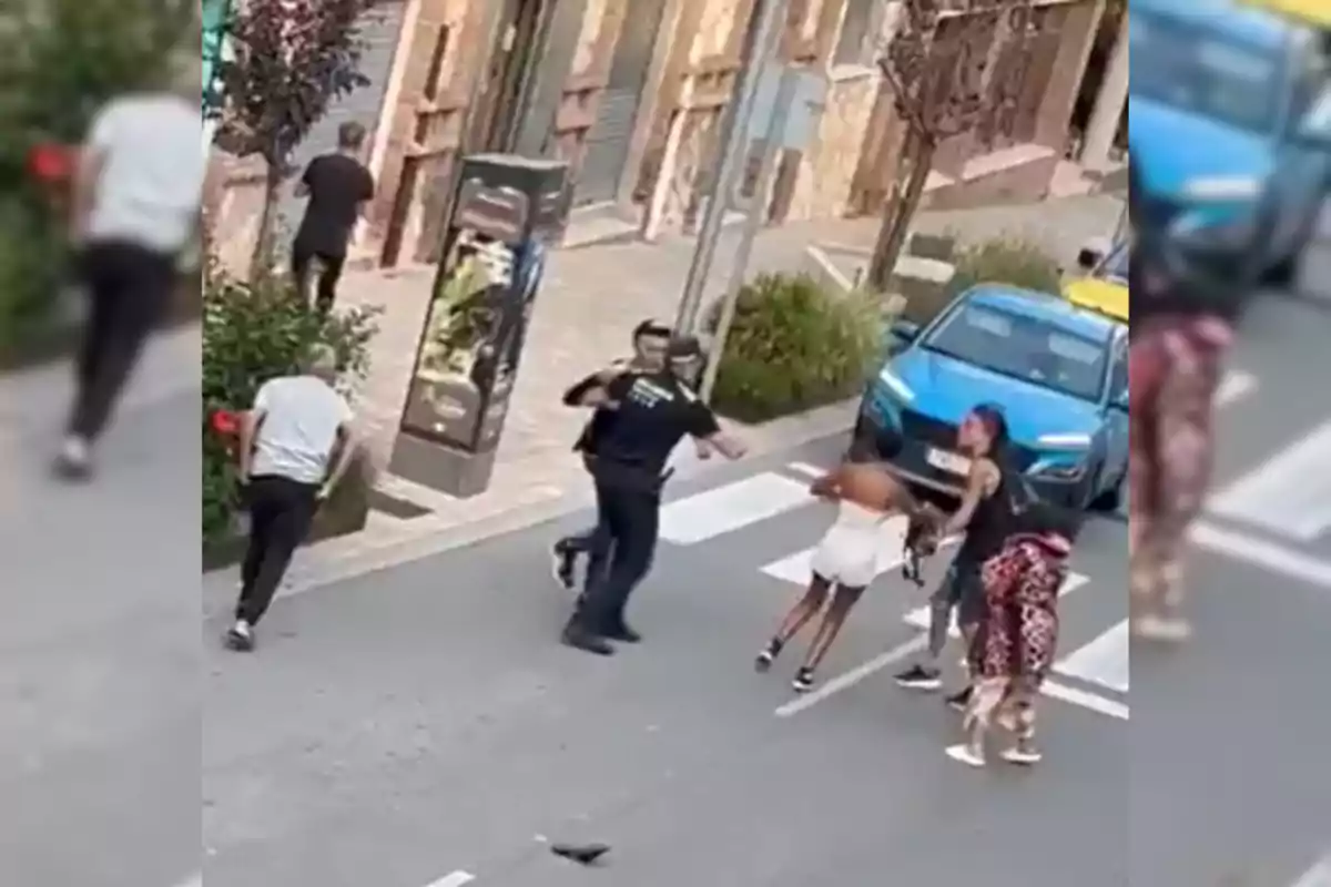 Una escena al carrer on diverses persones estan interactuant, amb un cotxe blau estacionat a prop.