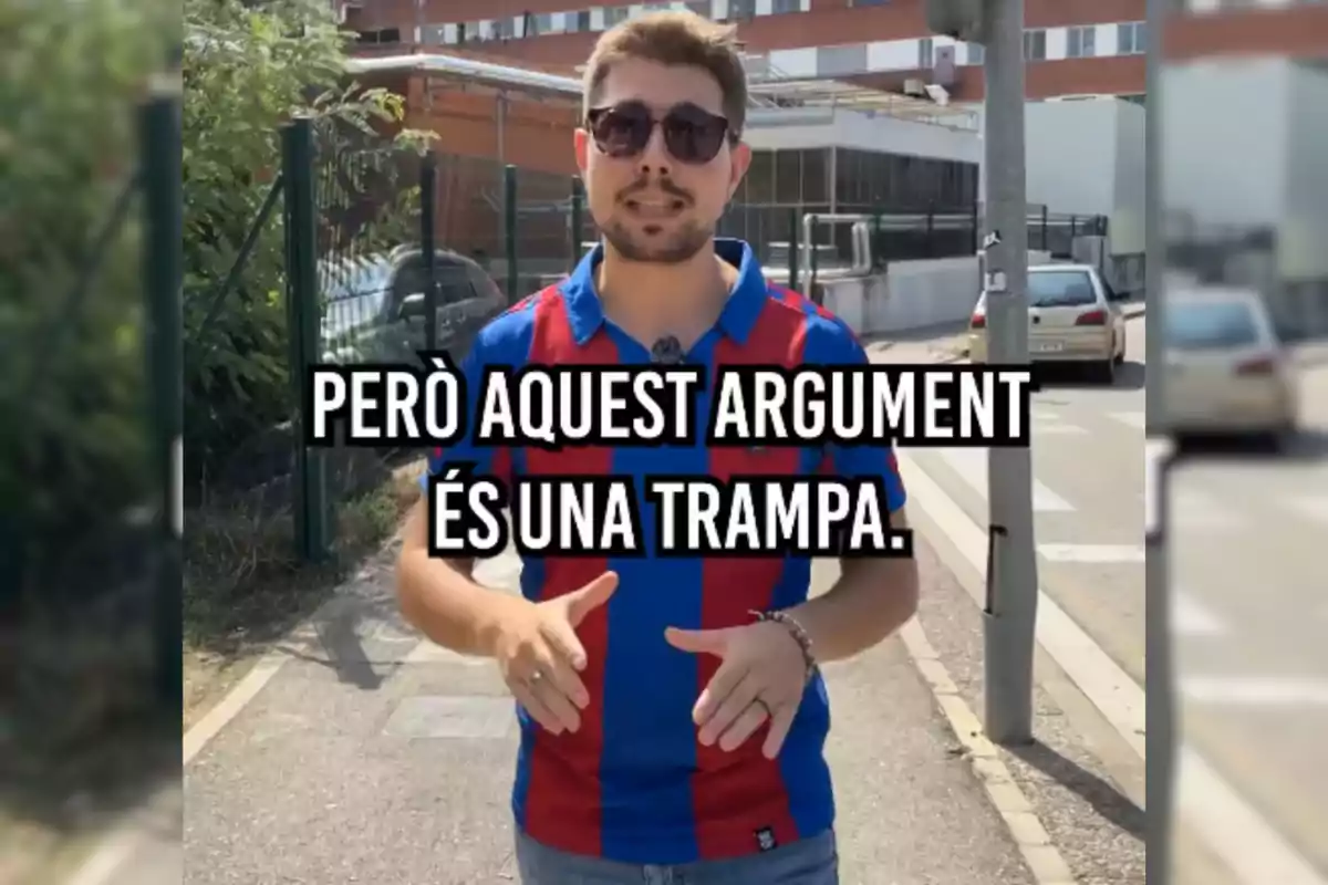 Un home amb ulleres de sol i una samarreta de ratlles vermelles i blaves està dreta en una vorera, amb un text en català que diu "PERÒ AQUEST ARGUMENT ÉS UNA TRAMPA."