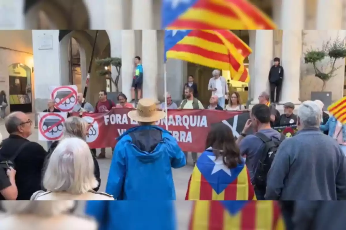 Una manifestació amb persones sostenint una pancarta vermella amb un missatge en català i banderes de Catalunya.