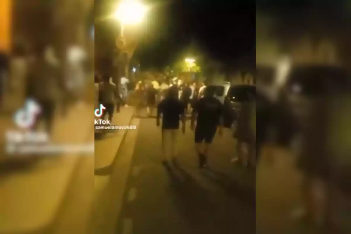 Una multitud de persones caminant per un carrer il·luminat per fanals durant la nit.