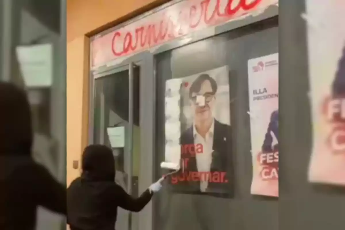 Una persona amb caputxa i guants està pintant sobre un cartell a la finestra duna carnisseria.