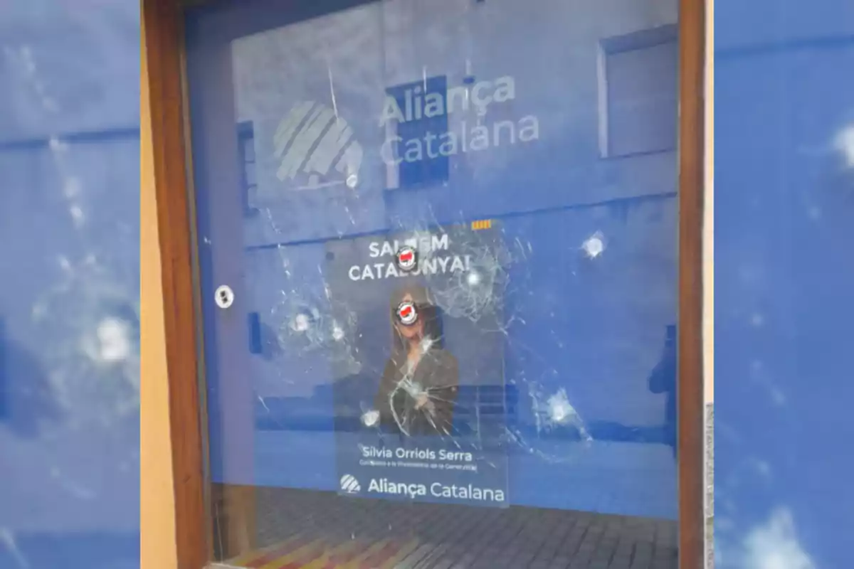 Una finestra amb un cartell d´Aliança Catalana que té diversos impactes visibles.