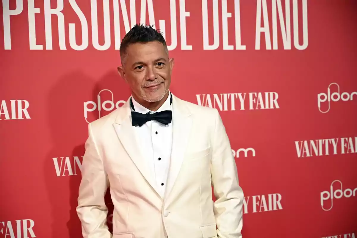 Alejandro Sanz amb esmòquing blanc i llacet negre posant en una catifa vermella amb fons de Vanity Fair Alejandro Sanz amb esmòquing blanc i llacet negre posant en una catifa vermella amb fons de Vanity Fair
