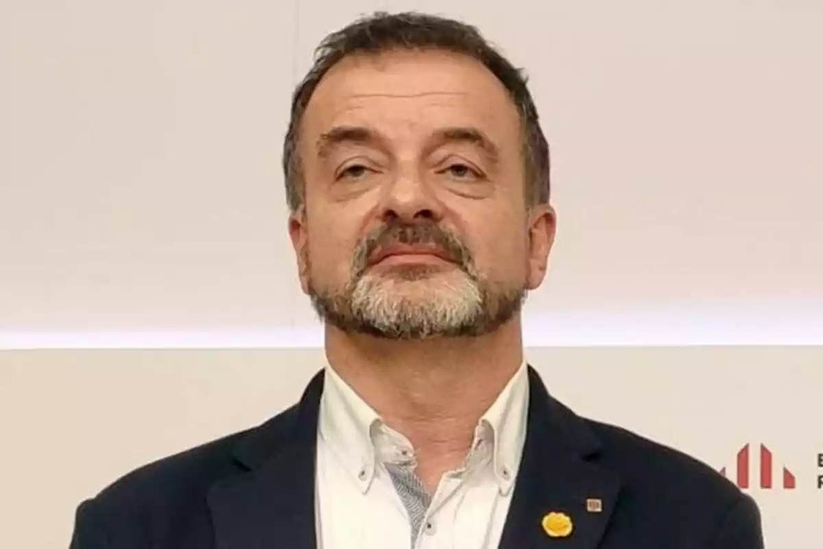 Un hombre con barba y cabello corto lleva un traje oscuro y una camisa blanca.