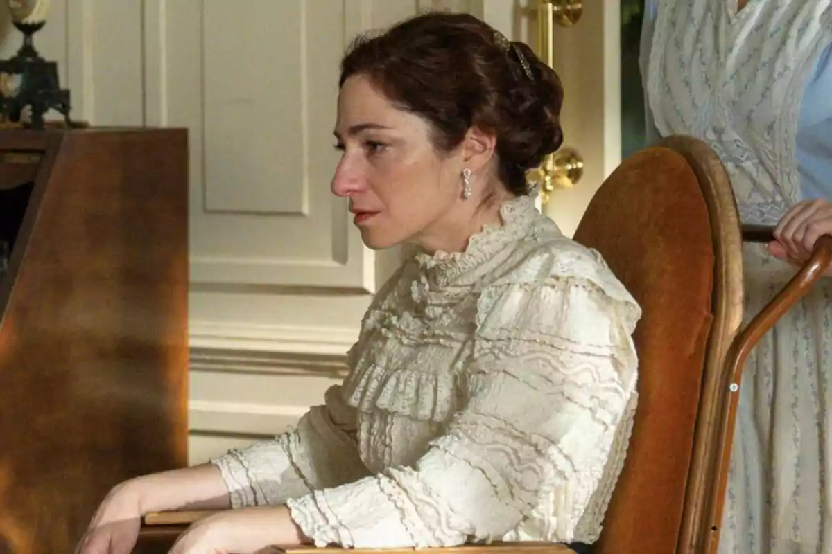 Alicia Moruno amb expressió seriosa està asseguda en una cadira, porta una brusa d'encaix d'estil antic i té els cabells recollits a La Promesa. Alicia Moruno amb expressió seriosa està asseguda en una cadira, porta una brusa d'encaix d'estil antic i té els cabells recollits a La Promesa.