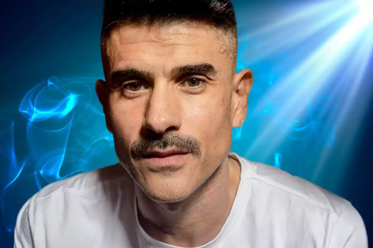 A man with a mustache and short hair looks at the camera with a lit blue background.