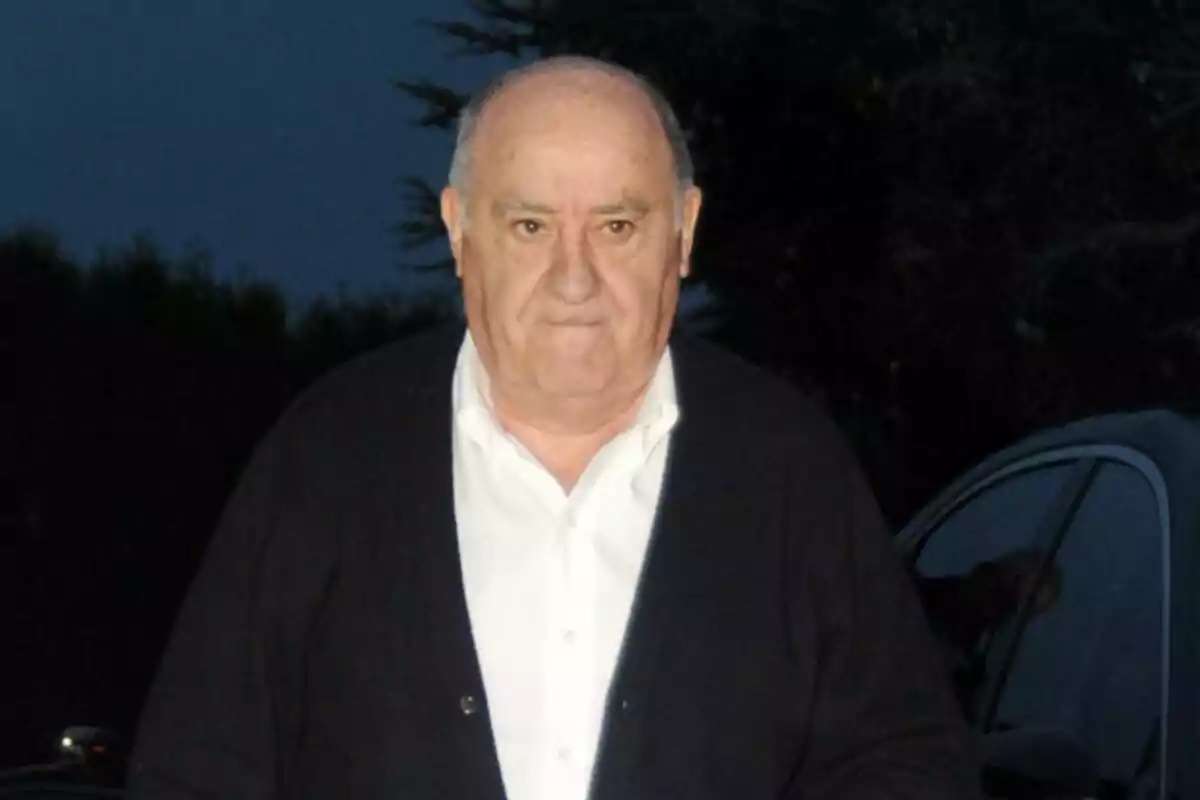 Amancio Ortega mayor, con camisa blanca y suéter oscuro de pie al aire libre por la noche. Amancio Ortega mayor, con camisa blanca y suéter oscuro de pie al aire libre por la noche.