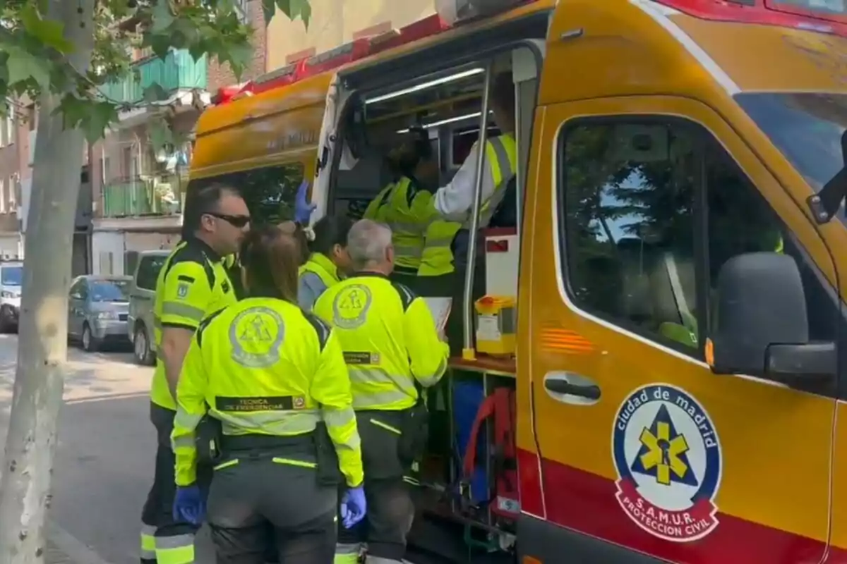 Un grup de paramèdics amb uniformes grocs és al costat d'una ambulància en un carrer de Madrid. Un grup de paramèdics amb uniformes grocs és al costat d'una ambulància en un carrer de Madrid.