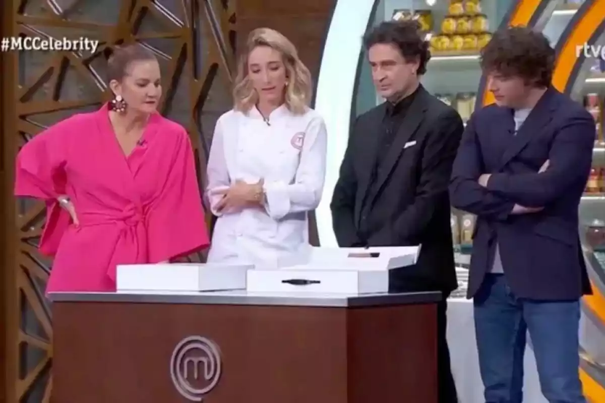 Un grup de persones format per Amelicious, Samantha Vallejo-Nágera, Pepe Rodríguez i Jordi Cruz està dret al voltant d'una taula en un plató de televisió, observant atentament alguna cosa davant d'ells a MasterChef. Un grup de persones format per Amelicious, Samantha Vallejo-Nágera, Pepe Rodríguez i Jordi Cruz està dret al voltant d'una taula en un plató de televisió, observant atentament alguna cosa davant d'ells a MasterChef.