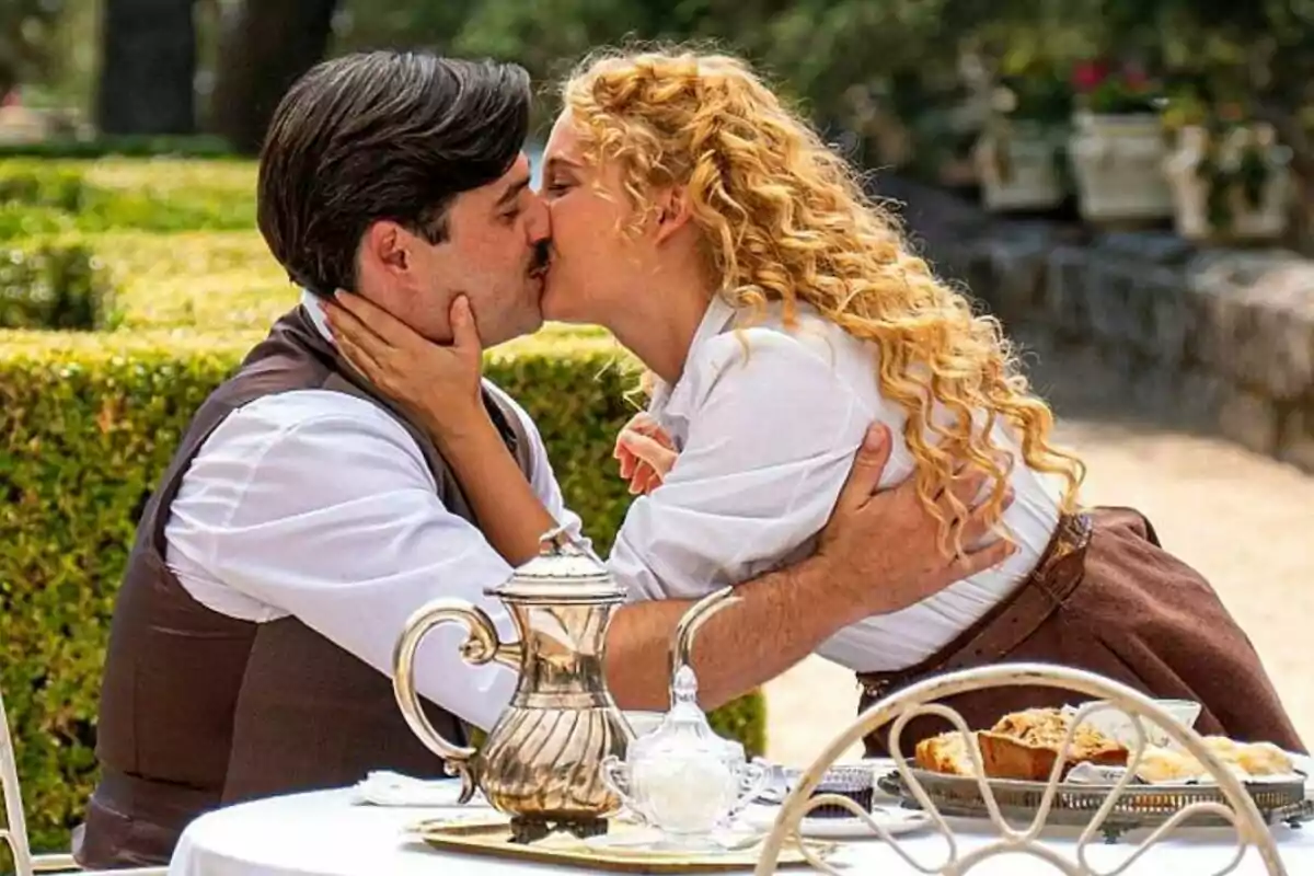 Arturo Sancho i Ana Garcés es besen apassionadament en un jardí mentre estan asseguts en una taula amb un servei de te a La Promesa.