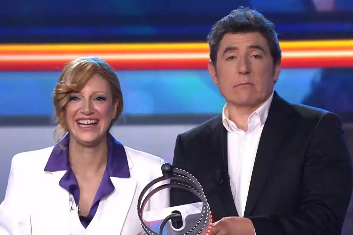 Ana Guerra i Manel Fuentes somriuen mentre sostenen el polsador de Tu Cara Me Suena en un escenari il·luminat.