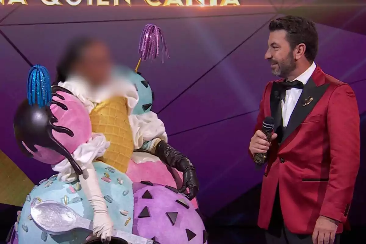 Ana Peleteiro disfressada de gelat amb cons i boles de colors és al costat d'un presentador que porta un vestit vermell i sosté un micròfon a Mask Singer.