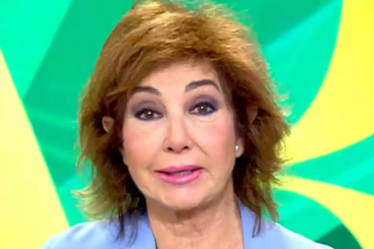 Ana Rosa Quintana con cabello castaño y maquillaje oscuro en los ojos, vistiendo una prenda azul, con un fondo de colores verdes y amarillos en El Programa de Ana Rosa.