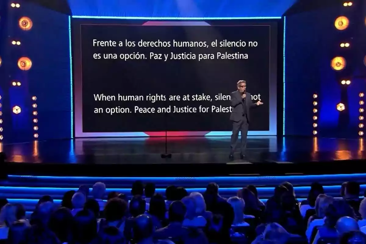 Andreu Buenafuente en un escenari de Futur Imperfecte amb una pantalla gran darrere que mostra un missatge sobre drets humans i justícia per a Palestina, mentre el públic observa. Andreu Buenafuente en un escenari de Futur Imperfecte amb una pantalla gran darrere que mostra un missatge sobre drets humans i justícia per a Palestina, mentre el públic observa.