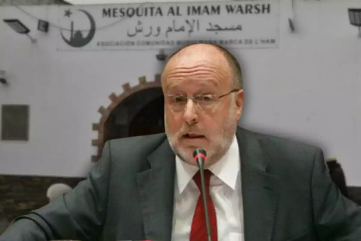 Un hombre con traje y corbata roja hablando frente a un micrófono con un fondo que muestra un edificio con un cartel que dice "Mesquita Al Imam Warsh".