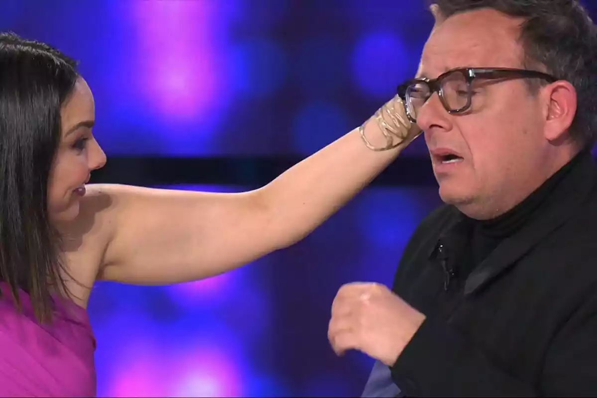 Chenoa toca la cara d'Àngel Llàcer amb expressió de sorpresa en un fons de llums blaves a Tu Cara Me Suena. Chenoa toca la cara d'Àngel Llàcer amb expressió de sorpresa en un fons de llums blaves a Tu Cara Me Suena.