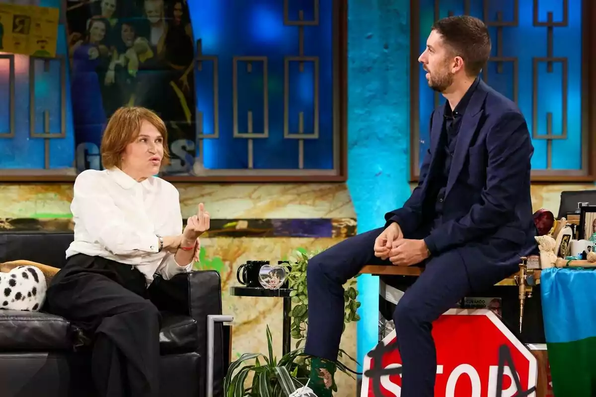 Antonia San Juan i David Broncano estan asseguts a La Revuelta, ella en un sofà negre i ell en un tamboret, tots dos semblen estar conversant en un ambient informal i acolorit. Antonia San Juan i David Broncano estan asseguts a La Revuelta, ella en un sofà negre i ell en un tamboret, tots dos semblen estar conversant en un ambient informal i acolorit.