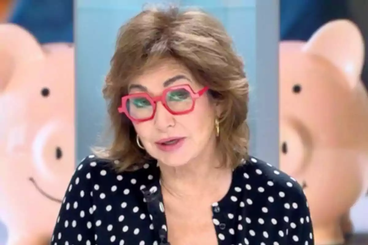 Ana Rosa Quintana con gafas rojas y blusa de lunares en un estudio de televisión con fondo de cerditos sonrientes en 'El programa de Ana Rosa'.