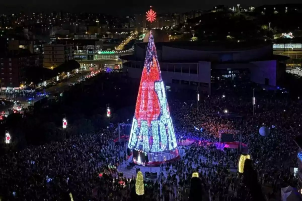 Una multitud es reuneix al voltant d'un gran arbre de Nadal il·luminat a una ciutat durant la nit.