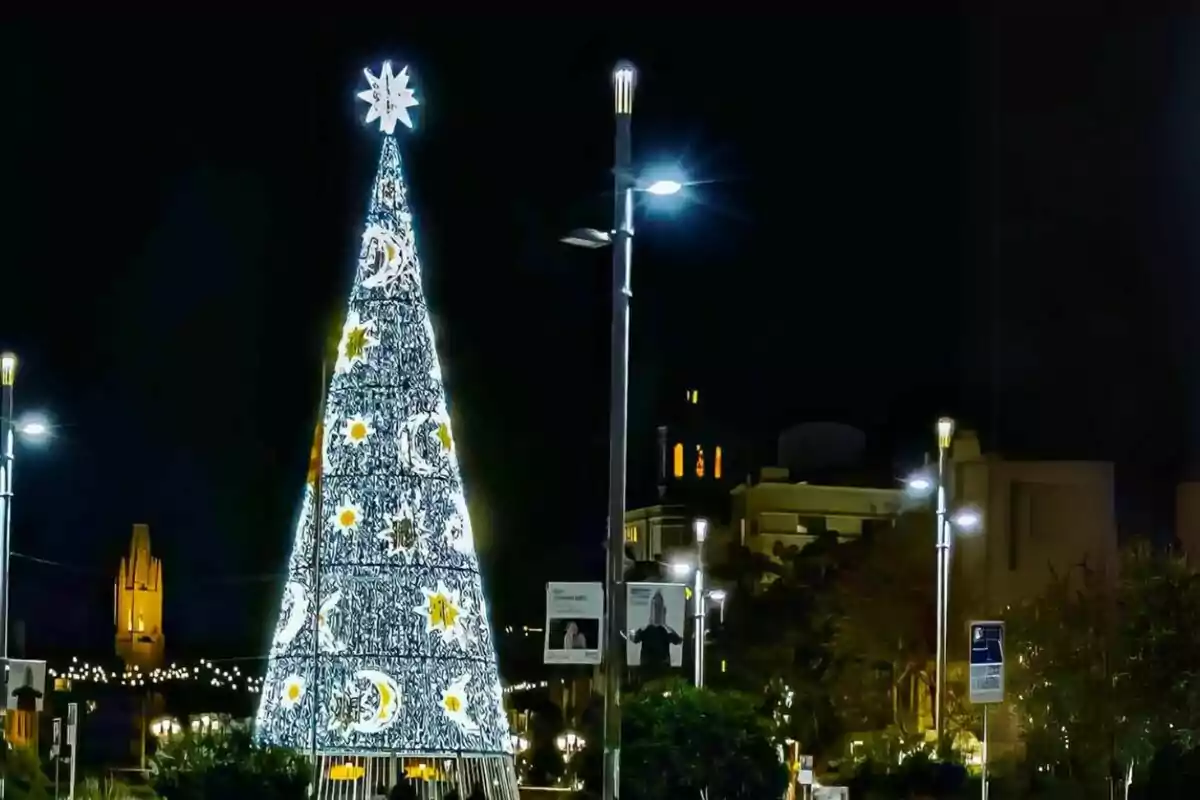 Un arbre de Nadal il·luminat amb decoracions d'estrelles i vidres en un entorn urbà nocturn.